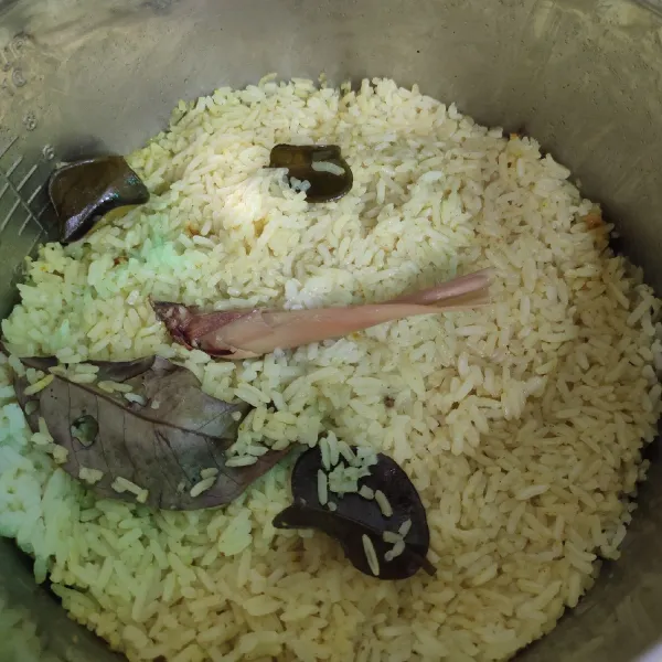 Pertama, masukkan beras, santan, kunyit, daun salam, serai, daun jeruk, garam, kaldu bubuk, dan daun pandan dalam panci rice cooker, tekan tombol "cook" masak sampai matang