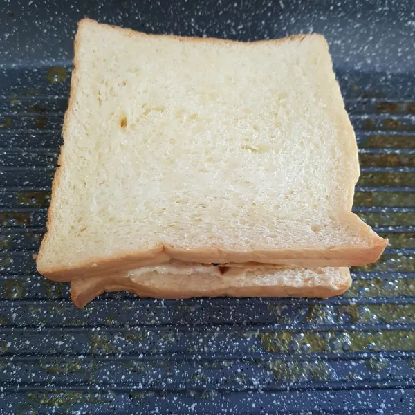 Kemudian tutup dengan 1 lembar roti yang sudah di beri bahan olesan. Kemudian panaskan pemanggang, beri secukupnya margarin. Panggang sandwich hingga kering kecoklatan