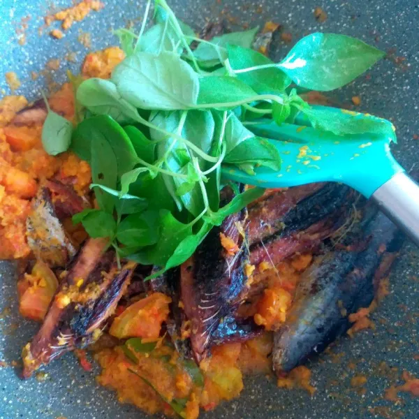 Masukkan ikan goreng dan kemangi, aduk rata hingga bumbu meresap dan air menyusut, koreksi rasa.
