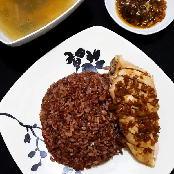 Lumuri ayam dengan campuran minyak bawang, sajikan dengan nasi merah hainan, sisa kaldu, dan sisa campuran minyak bawang untuk cocolan.