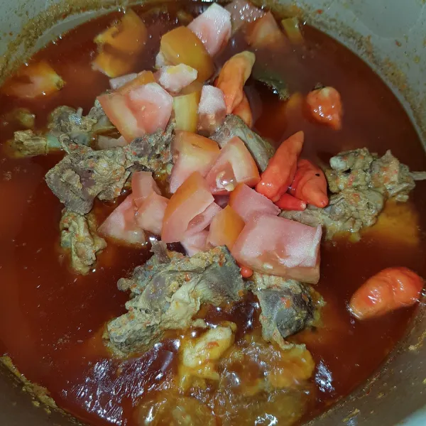 Setelah tulangan empuk, masukkan potongan tomat dan cabai rawit utuh. Aduk rata dan masak hingga kuah sedikit mengental