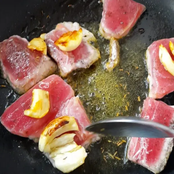 Taruh lah bawang putih di atas ikan tuna agar mengeluarkan flavor dan bawang putih tidak gosong.