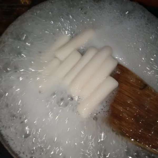 Didihkan air, lalu rebus kue beras sambil diaduk dengan spatula agar tidak menempel satu sama lain