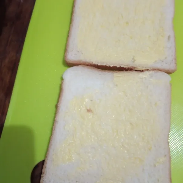 Olesi kedua roti dengan margarin.