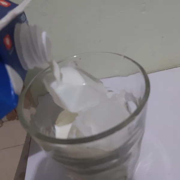 Pada gelas saji, siapkan es batu secukupnya, kemudian tuang 100 ml susu atau secukupnya ke dalam gelas.