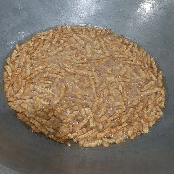 Iris tempe kecil-kecil lalu goreng sampai kering tak berbuih.