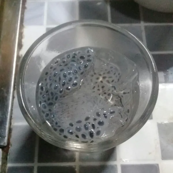 Masukkan es batu ke dalam gelas, tambahkan biji selasih yang sudah direndam air hangat.