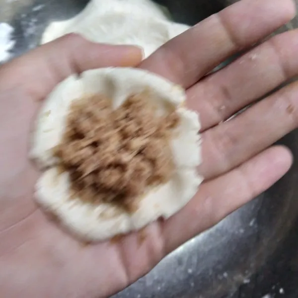 Setelah 15 menit, bagi adonan menjadi beberapa bagian atau bisa juga ditimbang dengan berat yang sama, ambil adonan lalu pipihkan di telapak tangan lalu isi dengan unti kelapa. Tutup kembali sambil dipadatkan.
