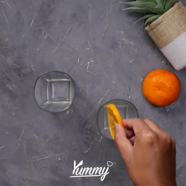 Siapkan gelas saji, lalu masukkan orange iris di bagian sisi gelas.
