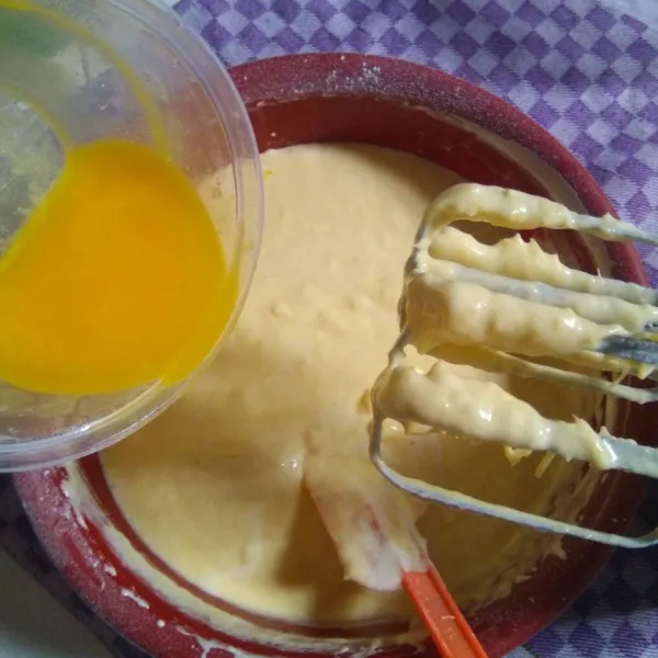 Masukkan campuran tepung ke dalam adonan tape, aduk balik menggunakan spatula. Kemudian masukkan margarin cair secara bertahap, aduk sampai tercampur rata, jangan sampai ada margarin yang mengendap di dasar adonan ya.