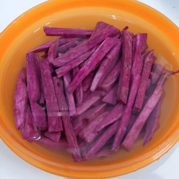 Kupas ubi. Potong memanjang sambil dimasukkan ke dalam air.