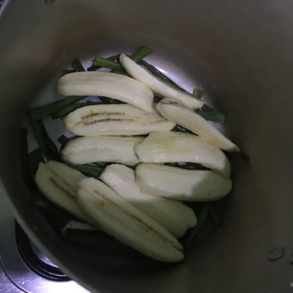 Potong daun pandan seukuran panci -+ 10cm. Tata dibagian dasar panci. Letakkan pisang dan tuang adonan santan.