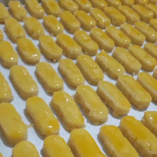 Oles rata permukaan kue dengan kuning telur dan taburi keju cheddar parut di atasnya. Lakukan sampai selesai.