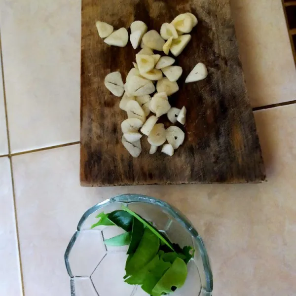 Iris tipis-tipis 4 buah bawang putih dan buang tulang daun jeruk.