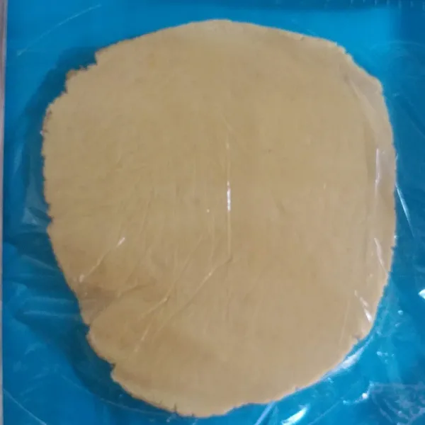 Taruh adonan di atas silpat. beri atasnya plastik lagi, Lalu gilas dengan rolling pin ketebalannya 1/2 cm.