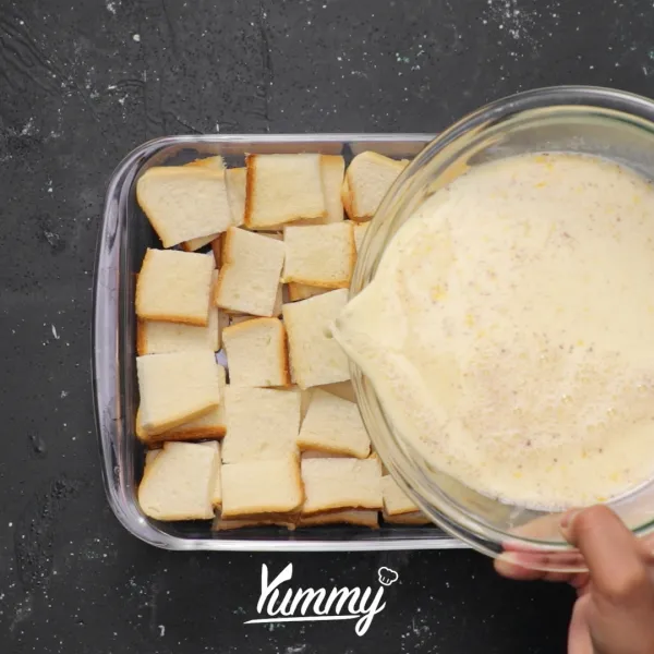 Letakkan roti tawar dalam pinggan anti panas hingga penuh lalu tuangkan campuran susu dan telur ke dalamnya.
