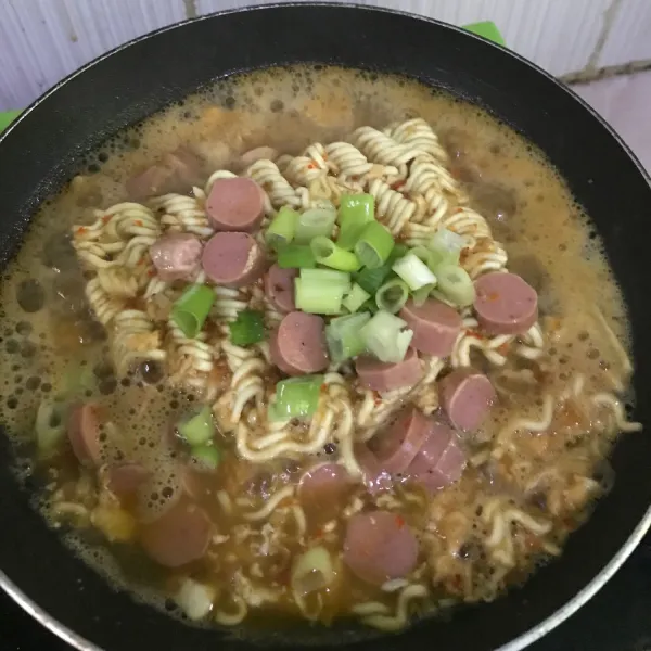Setelah mie agak empuk, masukkan sosis dan daun bawang.
