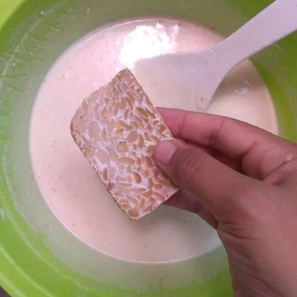 Celupkan tempe satu per satu ke dalam larutan tepung dan bumbu.