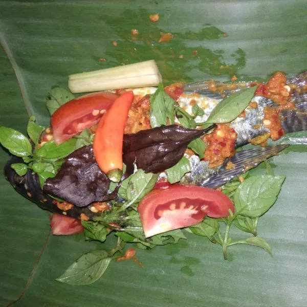 Ambil daun pisang taruh daun kemangi,salam, sereh lalu ikan nila, Tambahkan bumbu daun salam irisan tomat dan cabe rawit utuh.