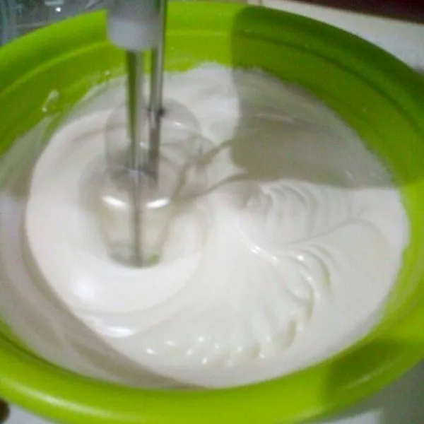Masukkan gula sedikit2 secara bertahap (3x), setiap memasukkan gula kocok dulu dengan mixer sampai tercampur rata baru masukkan lagi. Kocok sampai putih mengental, kaku & berjejak.