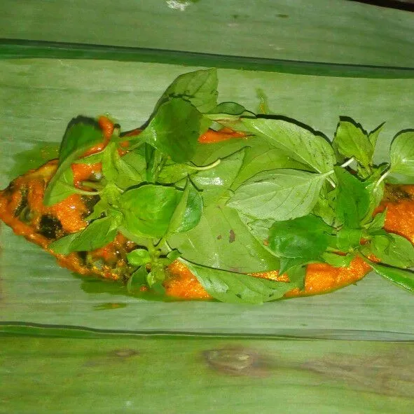 Ambil daun pisang letakan ikan diatasnya beri daun salam dan daun kemangi lalu bungkus sematkan ujungnya dengan lidi.