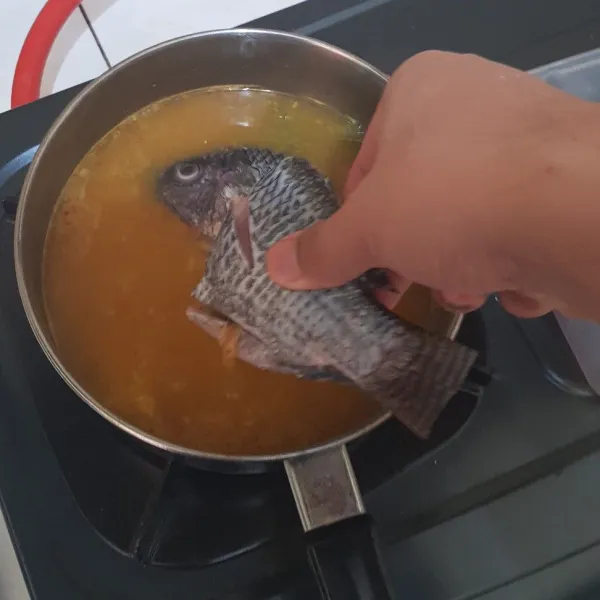 Masukkan ikan nila yang telah di potong dan di cuci bersih dan masak dengan api sedang dan usahakan pancinya ditutup hingga ikan matang.