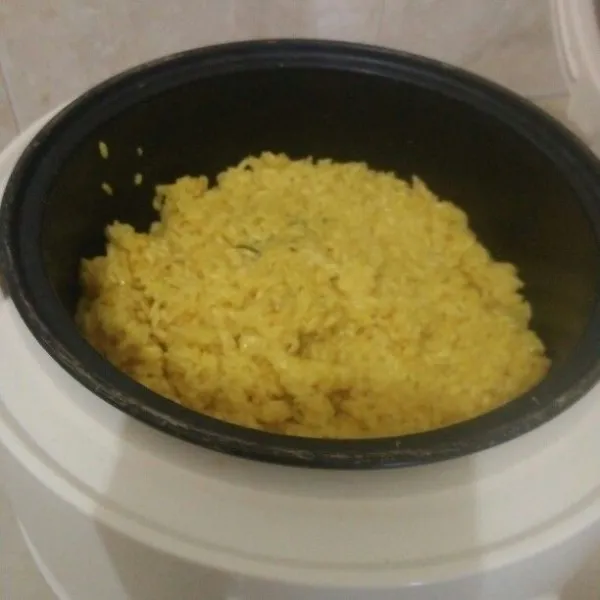 Setelah airnya menyusut, masukkan beras yang sudah menyusut ke dalam rice cooker dan tambahkan air sedikit demi sedikit sambil sering diaduk agar nasi tidak keras.