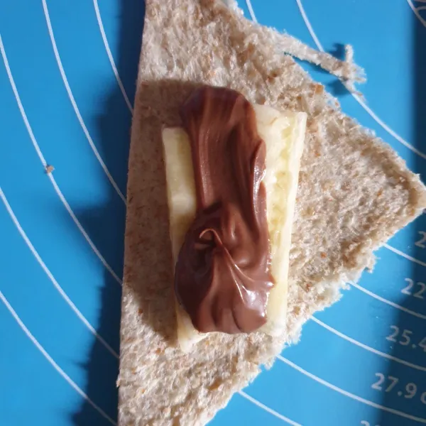 Tambahkan potongan pisang dan selai coklat pada salah satu belahan roti.