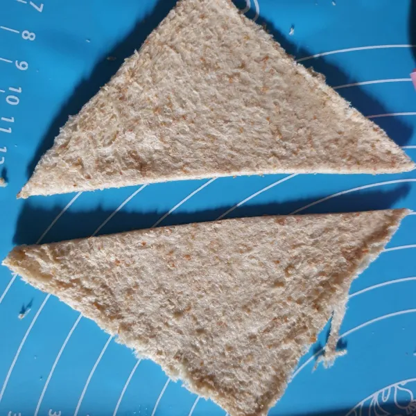 Potong roti secara diagonal hingga menjadi 2 belah roti berbentuk segitiga.