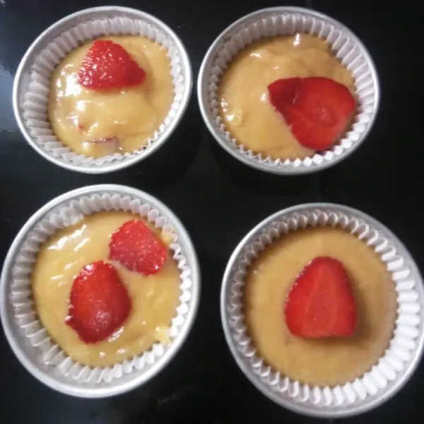 Tuang kedalam cup muffin, lalu beri topping buah strawberry di atas adonan muffin.