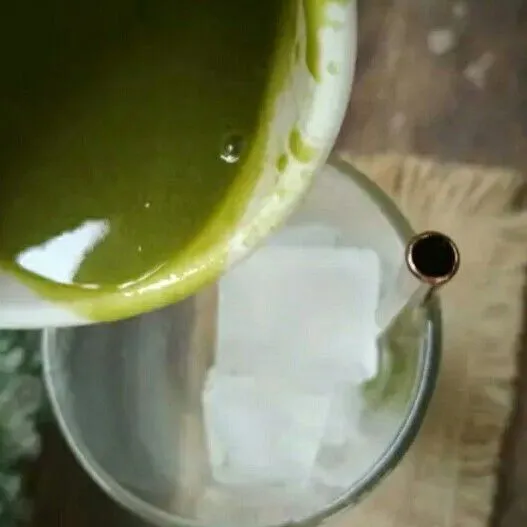 Tuang matcha latte kedalam gelas yang berisi batu es.