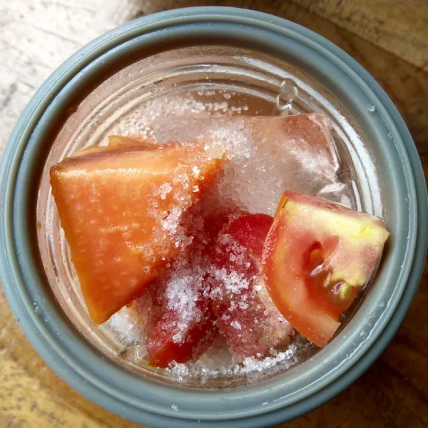 Masukkan potongan tomat, pepaya, es batu dan gula pasir ke dalam blender. Tambahkan 100 ml air.