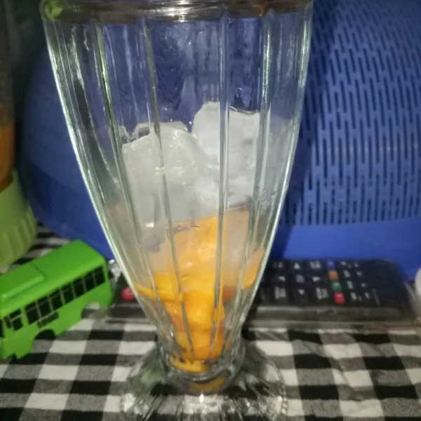 Siapkan gelas saji, tata potongan buah mangga didasar gelas dan tambahkan es batu.