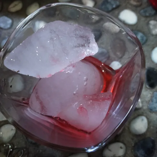 Siapkan gelas, beri es batu. Beri sirup.