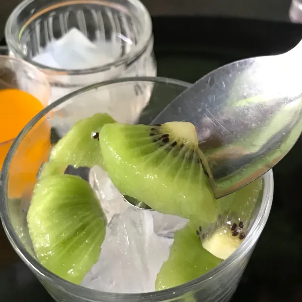 Masukkan es batu lalu buah kiwi yang telah dipotong ke dalam gelas.