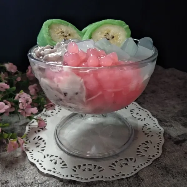 Dalam gelas tata es batu, potongan pisang, vla ketan hitam, sagu mutiara dan nata de coco. Siram dengan kental manis. Siap dinikmati.