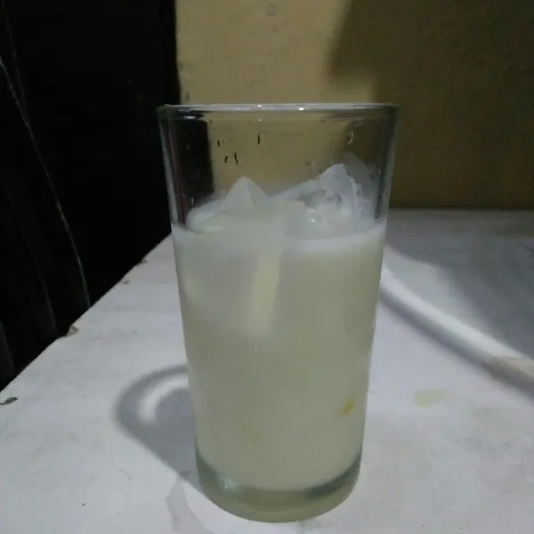 Tuangkan susu cair plain ke dalam gelas berisi es batu.