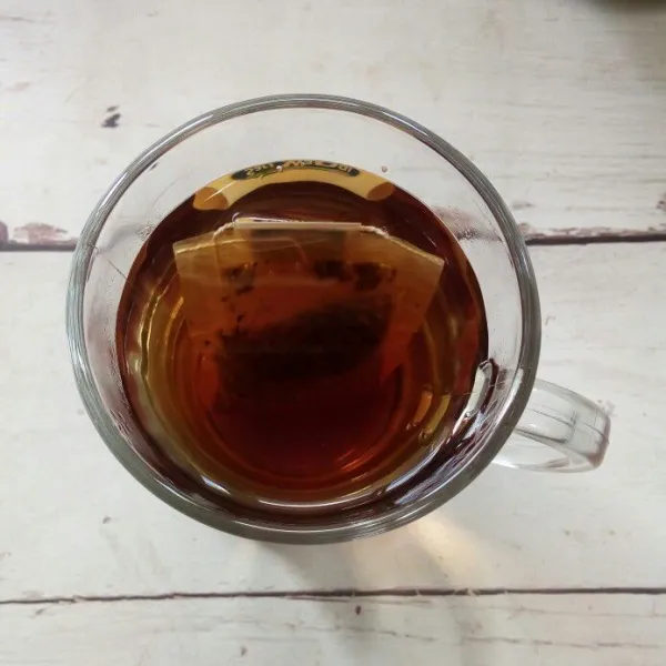 Siapkan wadah/pitcher, seduh kantong teh dengan air panas hingga berwarna pekat. Biarkan hingga hangat.