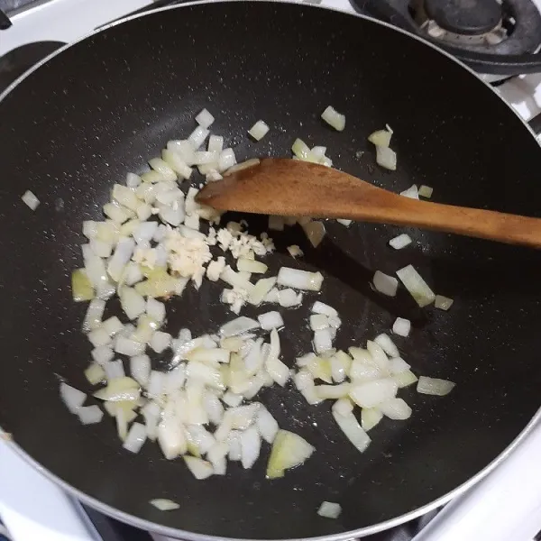 Panaskan minyak dari kaleng tuna, tumis bawang bombay hingga harum, lalu masukkan bawang putih, masak hingga layu.