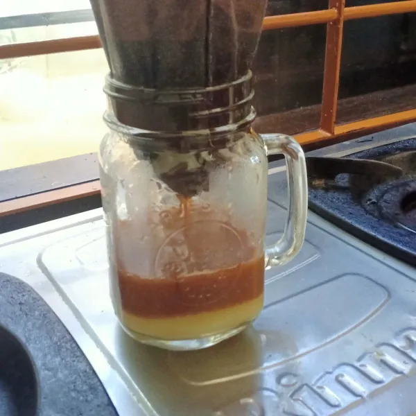 Tuangkan kopi panas dalam saringan ke gelas yang telah diberi SKM