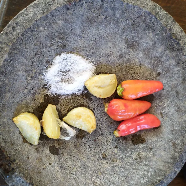 Siapkan cabe dan garam di cobek. Angkat bawang putih jika sudah agak kecoklatan.