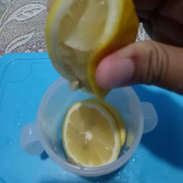 Potong lemon menjadi dua dan taruh di wadah dan peras.