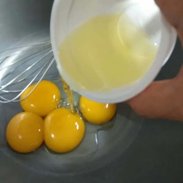 Membuat adonan kuning telur: gunakan whisk, aduk kuning telur dengan minyak hingga rata. Tambahkan air lemon, aduk rata.