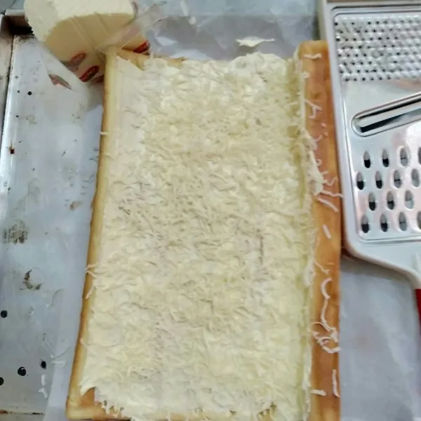 Buka gulungan, olesi dengan buttercream dan keju parut.