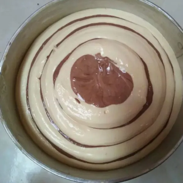 Siapkan loyang bulat D 18 cm oles tipis dengan margarine lalu mulai menuang 3  sdm adonan ca coklat dibagian tengah loyang,  lalu di seling tuang 3 sdm adonan putih tepat di tengah adonan coklat, lakukan begitu terus sampai adonan habis sampai membentuk motif lingkaran.
