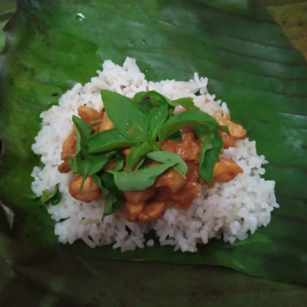 Siapkan daun pisang. Ambil 2 sdm nasi kemudian letakkan ayam dan daun kemangi. Bungkus memanjang mirip lontong.