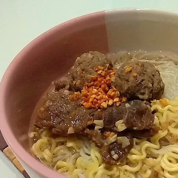 Rebus bihun daan mie kuning, tata di dalam mangkuk bersama dengan sup sapi. Taburi sedikit bawang putih goreng sebagai hiasan di atasnya.