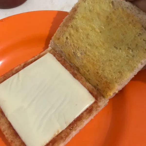 Oleskan margarine pada bagian roti yang menutupi keju, dan oleskan saus sambal pada bagian sebelahnya.