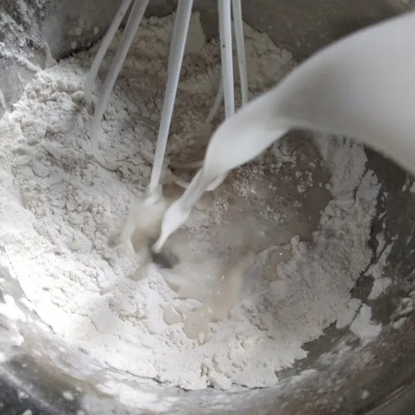 Tuang santan hangat sedikit demi sedikit ke dalam adonan tepung, sambil diaduk dengan whisk hingga rata.