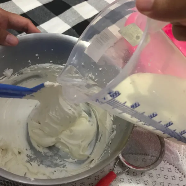Tuangkan susu cair secara bertahap (menjadi dua tahap) serta aduk lipat menggunakan spatula sampai semuanya tercampur.